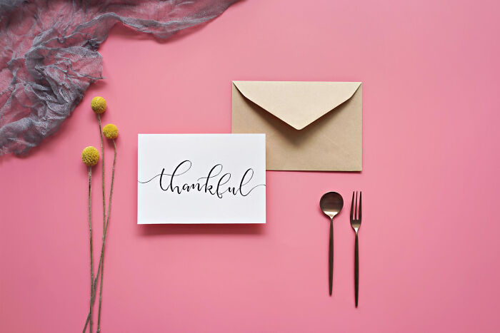 Thankful card with an envelope, beside a fork and spoon, on a pink background, representing cheap creative alternatives.