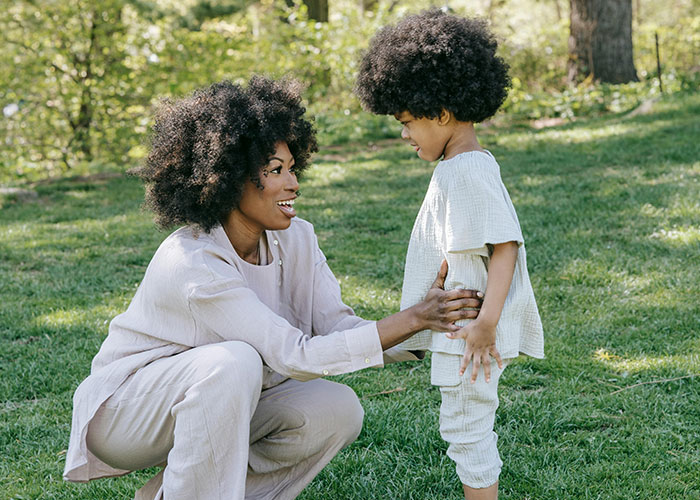 Mom engaging in gentle parenting with her child in a sunny park, both smiling and wearing light outfits.