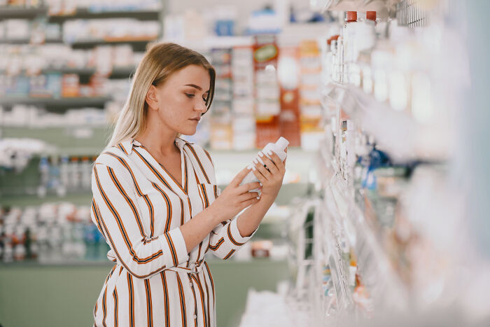 Woman in a store aisle examining a bottle, representing affordable alternatives to expensive products.