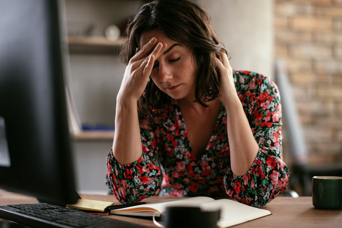 Woman in floral dress, at desk, looking stressed about neighbors driving in her yard.