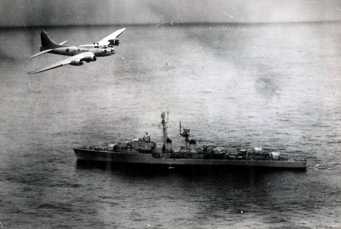 Historic airplane flying over a warship at sea, showcasing cool Wikipedia history articles.