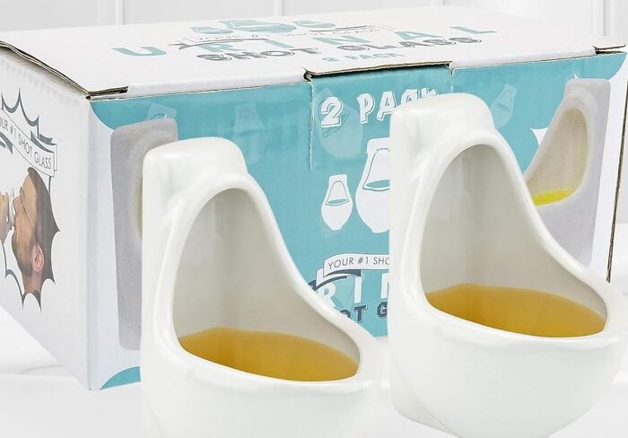 Novelty urinal-shaped shot glasses in front of a colorful box, exemplifying toilet humour in barware design.