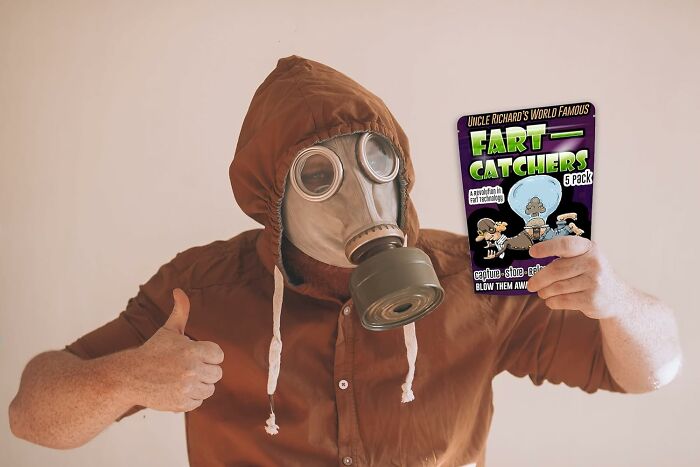 Person in gas mask holding &ldquo;Fart Catchers&rdquo; pack, giving thumbs up, illustrating toilet humour concept.