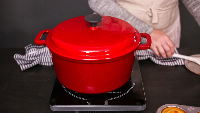 Red Dutch oven on stovetop, an affordable alternative to pricey cookware, with a person preparing food nearby.