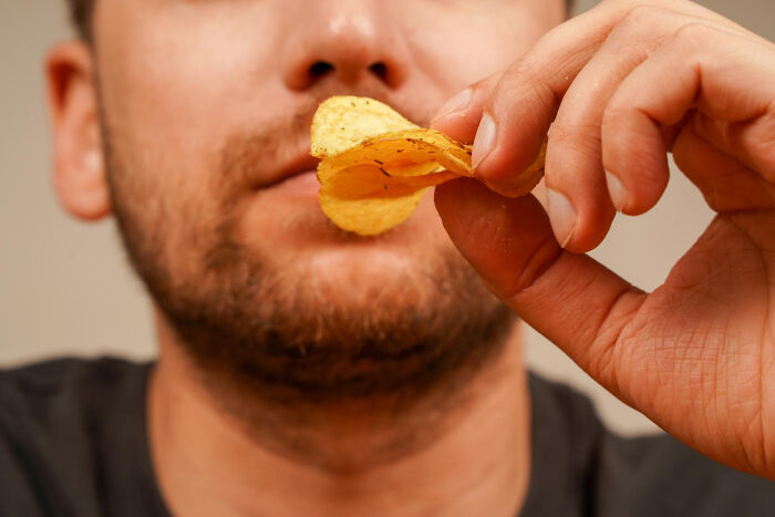 Close-up of a man holding a chip, exemplifying cheap versions of snacks that surpass pricier options.