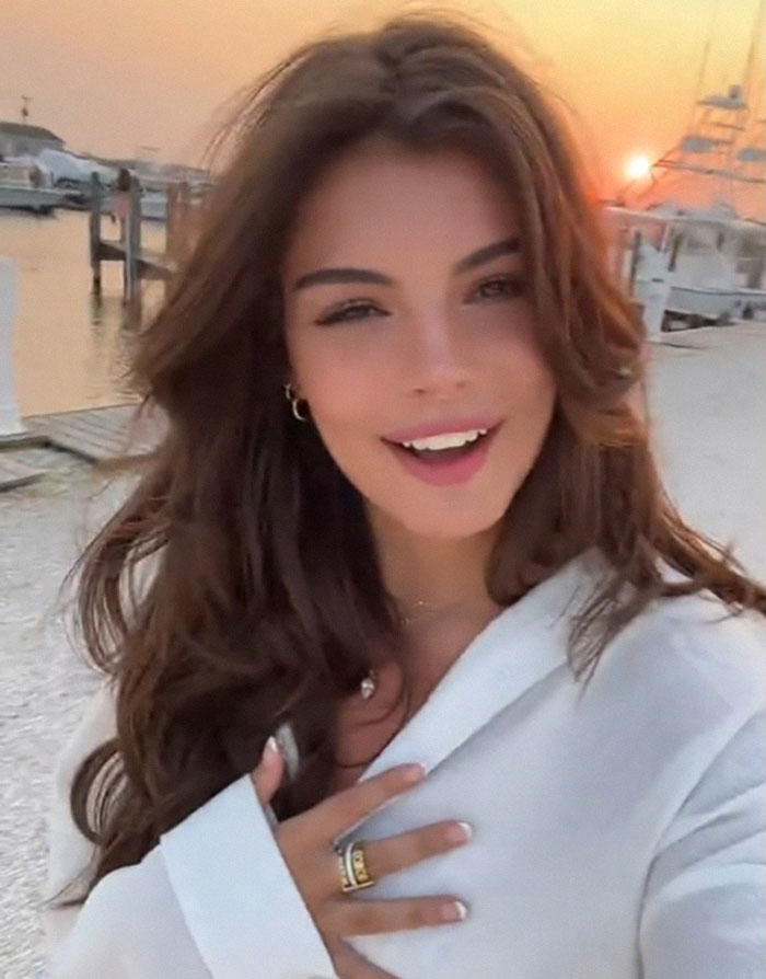 A smiling woman in a white top by the seaside at sunset, capturing a romantic moment.