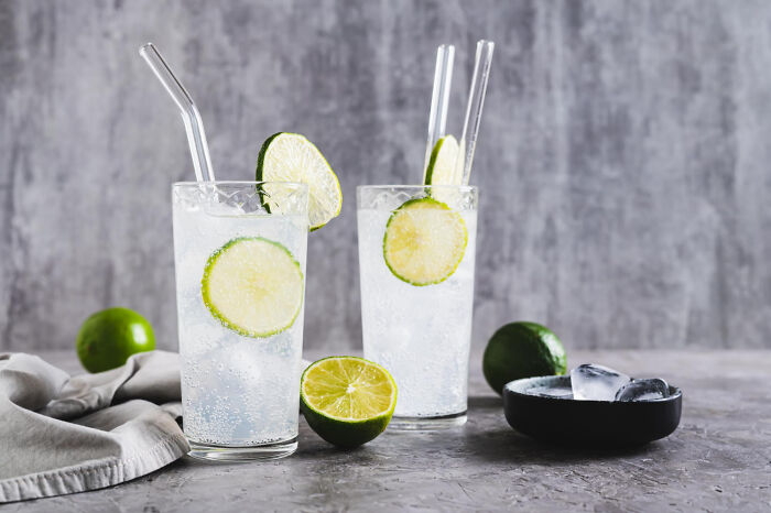 Two glasses of cheap lime soda with ice, garnished with lime slices, on a grey background.