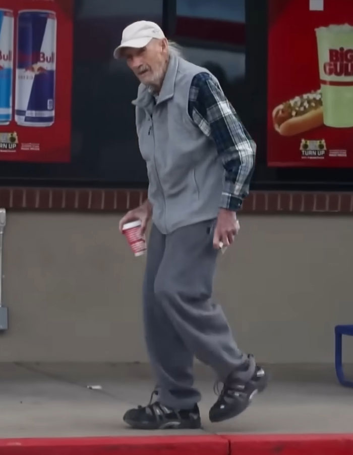 Elderly man in casual wear holding a drink, walking outside a store with energy drink ad.