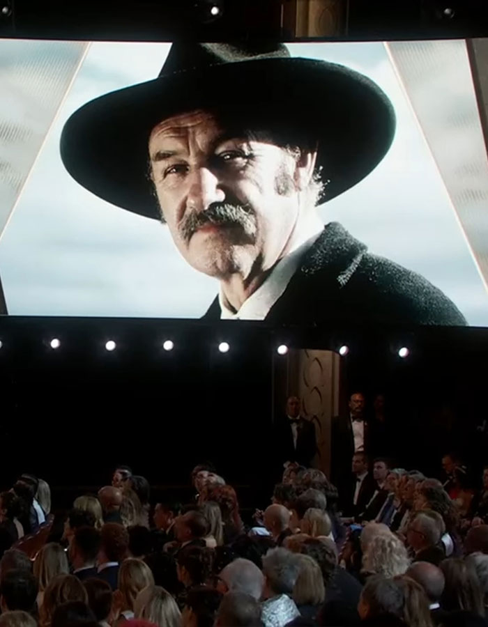 A large screen displays an image of a man in a cowboy hat at an event, with an audience seated below.