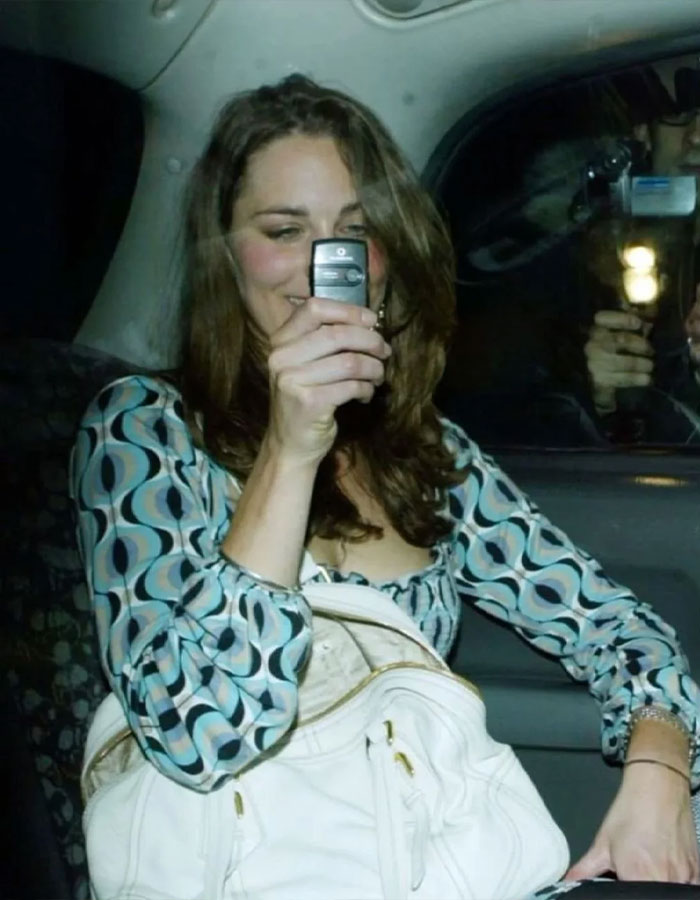 Woman smiling in a car, holding a phone, showcasing stunning pre-princess style with a patterned blouse and white bag.