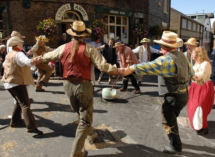 People in traditional costumes dancing in a circle during a street festival outside Lewes Arms pub.