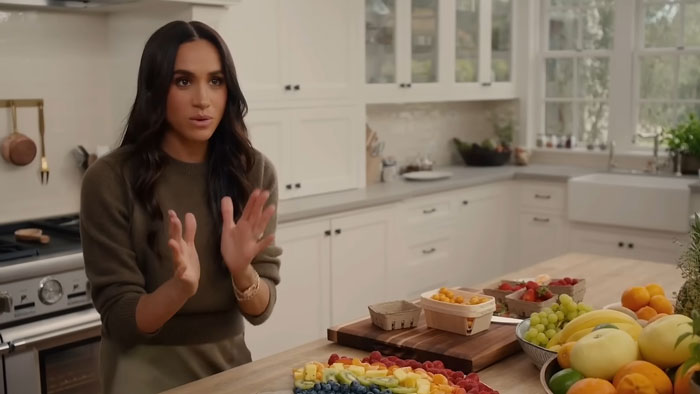 Meghan Markle in a kitchen discussing a project with assorted fruits, related to her work on a Netflix show.