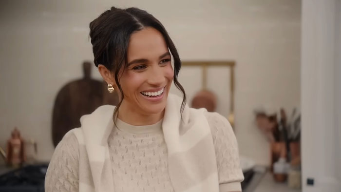 Smiling Meghan Markle on Netflix set, wearing a patterned top and scarf, showcasing her friendly demeanor.