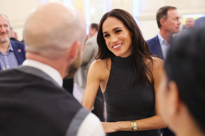 Person in a sleeveless dress smiling in conversation at a social event, highlighting a friendly interaction.