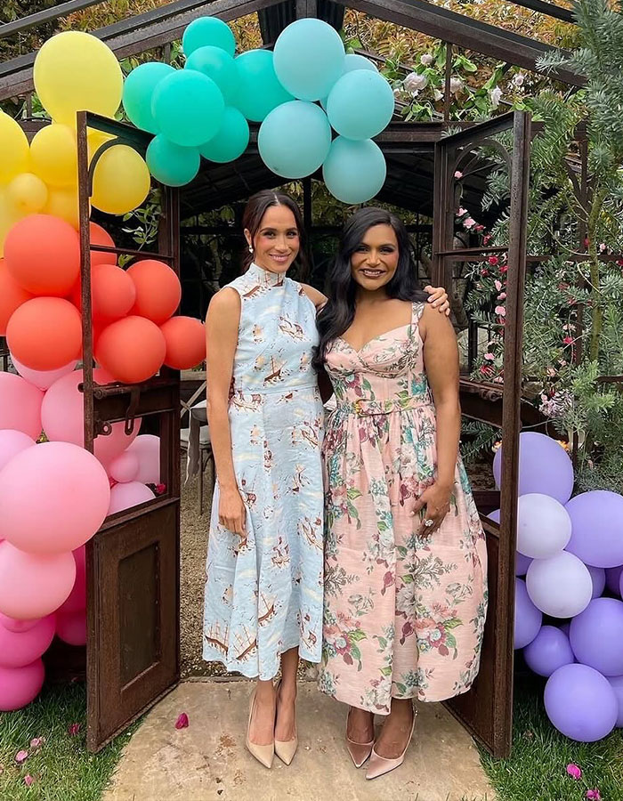 Two women in floral dresses, standing together at a garden party with colorful balloons.