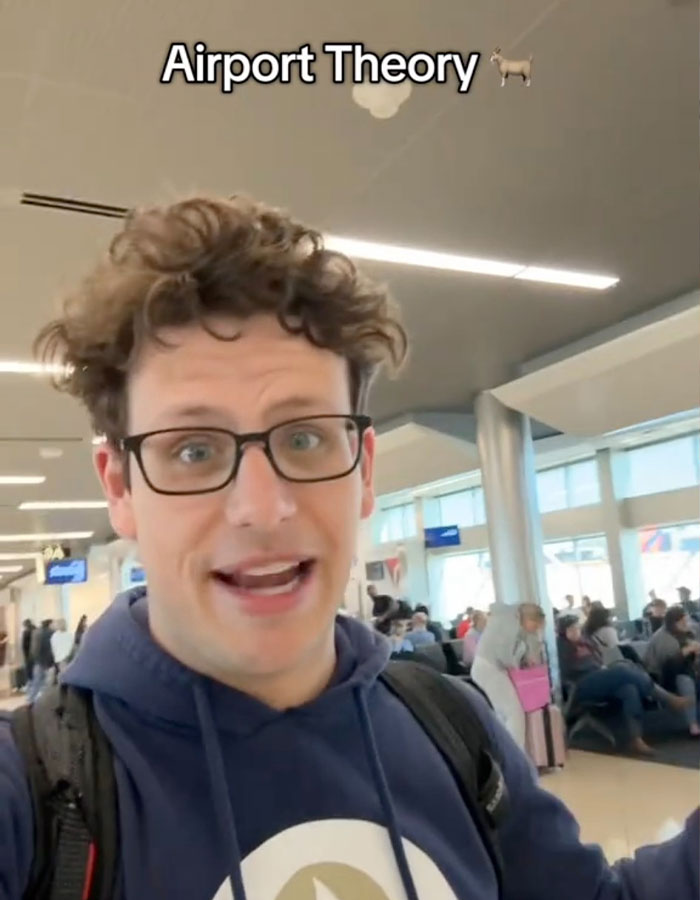 Man in an airport discussing the viral "Airport Theory" trend, wearing glasses and a blue hoodie.