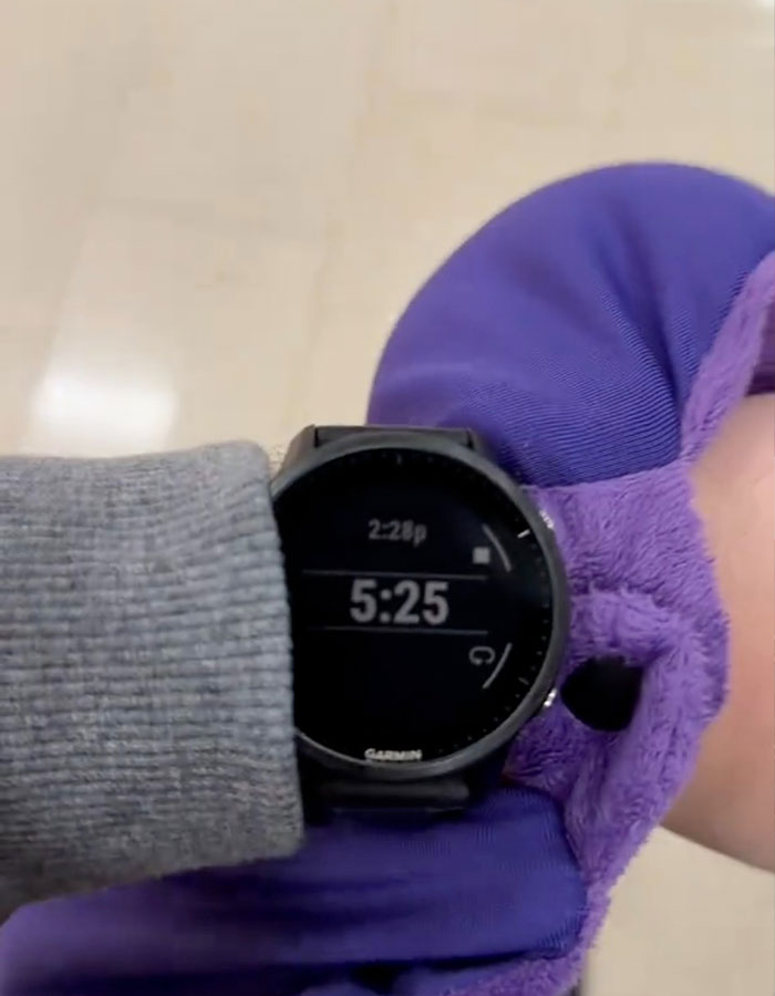 Watch showing 5:25 with an unseen hand wearing a purple sleeve, related to the viral &ldquo;Airport Theory&rdquo; trend.