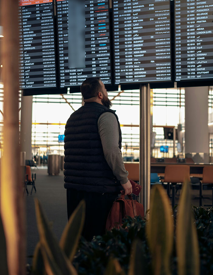 Passenger in puffer vest checking airport departure board; possibly impacted by viral airport trend.