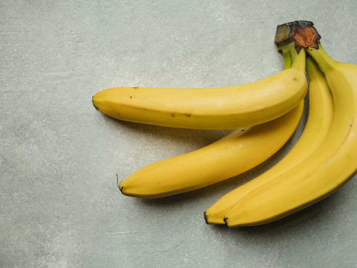 A bunch of ripe yellow bananas on a gray background, ideal for exploring cool Wikipedia articles about fruit.