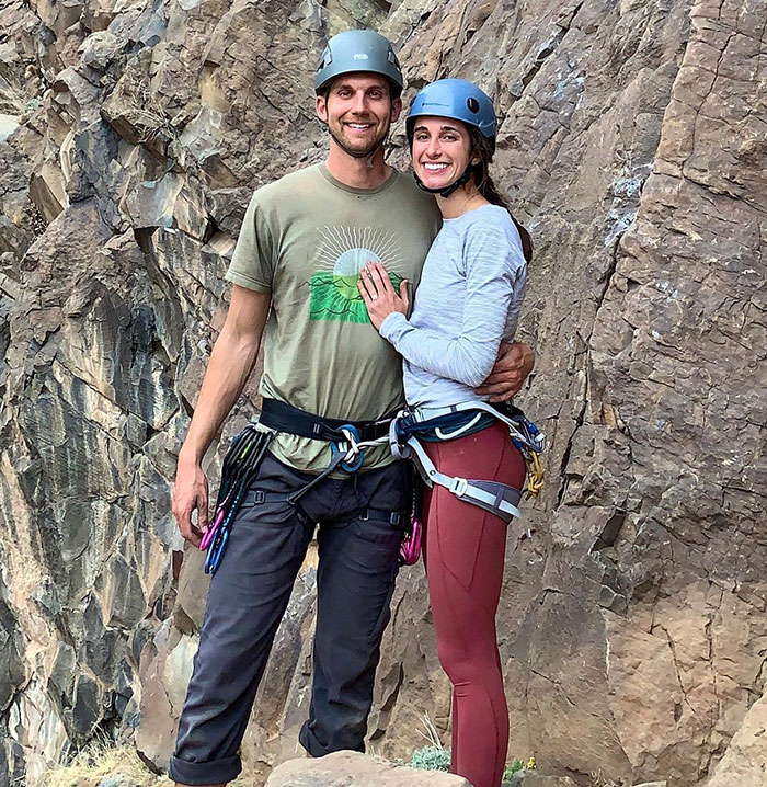 A couple with climbing gear smiling by a rock face.