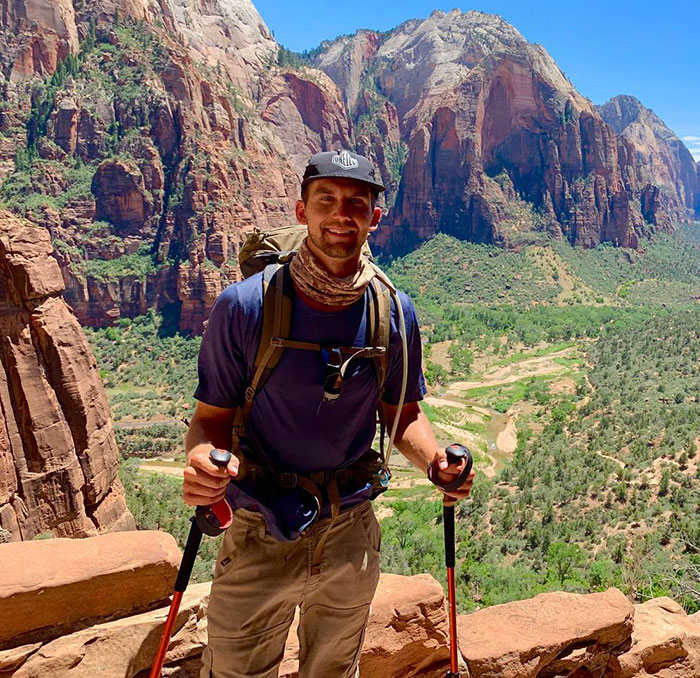 A man hiking with poles in a scenic mountain setting, wearing a hat and backpack.