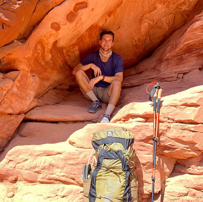 YouTube star sitting in red rock alcove with hiking gear.