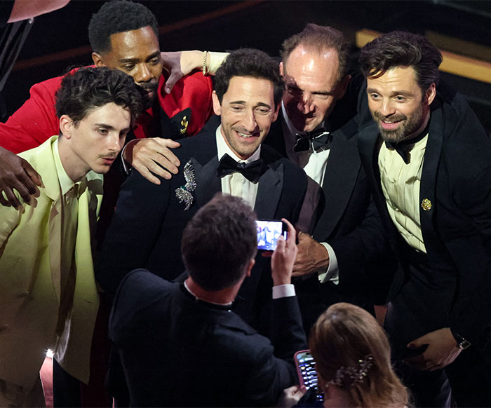 Group of men in suits posing for a photo, smiling behind the scenes at Oscars 2025.