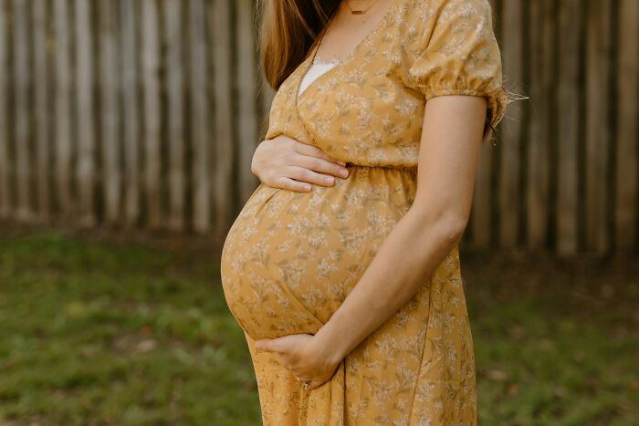 Pregnant woman in a yellow dress standing outside, hands gently on her belly, related to wedding objection stories.