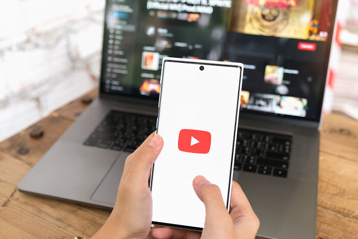 Hands holding a smartphone with the YouTube logo, laptop open in the background, highlighting valuable memberships.