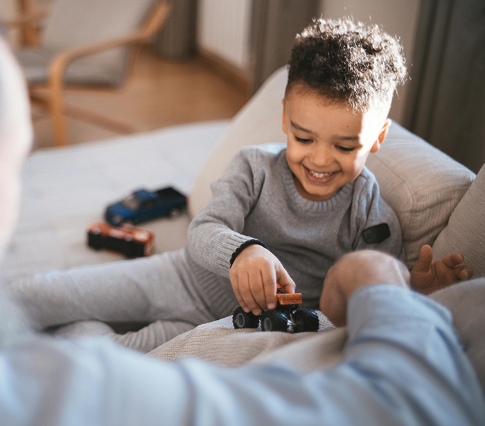 Child happily playing with toy cars on a sofa, interacting with a friend, creating a joyful holiday atmosphere.