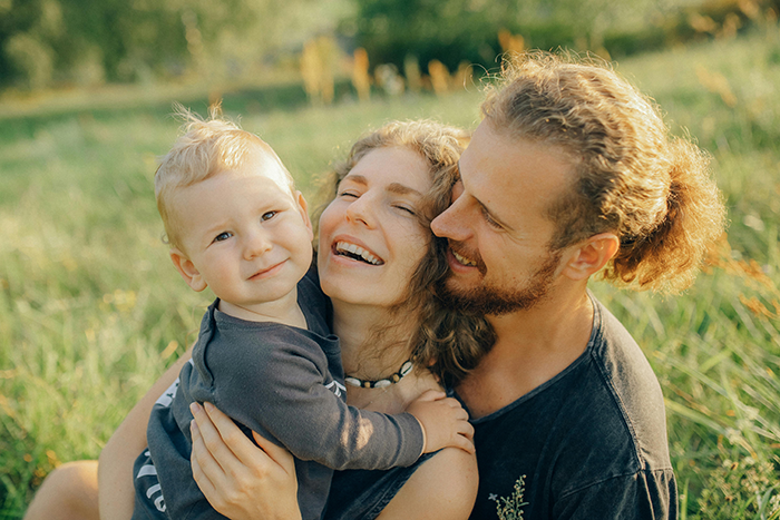 Happy couple with child enjoying a holiday outdoors, highlighting childfree friend\'s upset feelings.