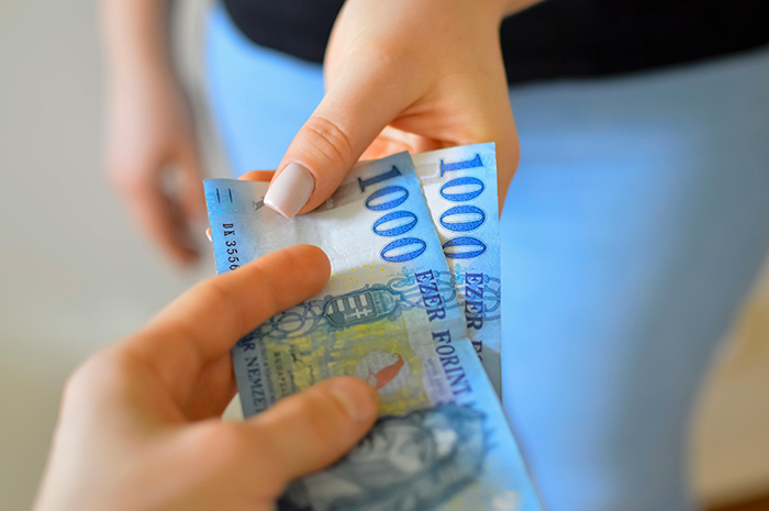 Two people exchanging 1000 forint bills, symbolizing a financial disagreement.