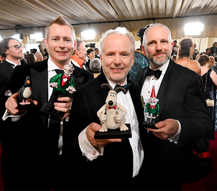 Three men in tuxedos holding animated character figures at Oscars 2025 behind the scenes.