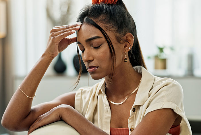 Woman looking stressed, considering care for stepsiblings if needed, sitting indoors in a thoughtful pose.