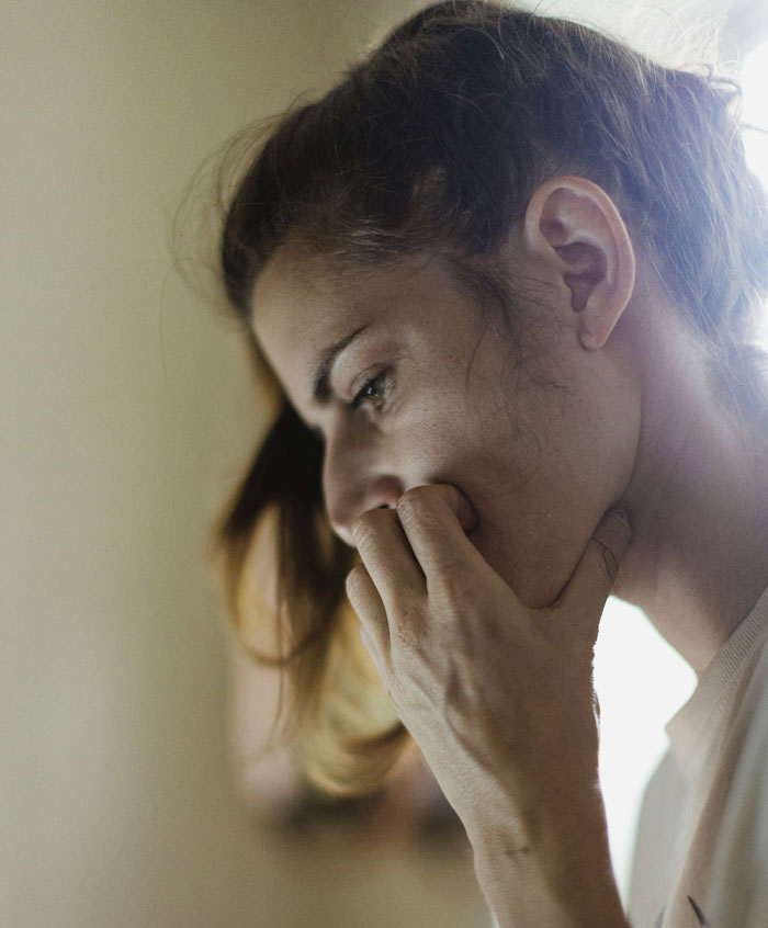 Person looking thoughtful, hand on mouth, contemplating sterilization decision amid partner disagreement.