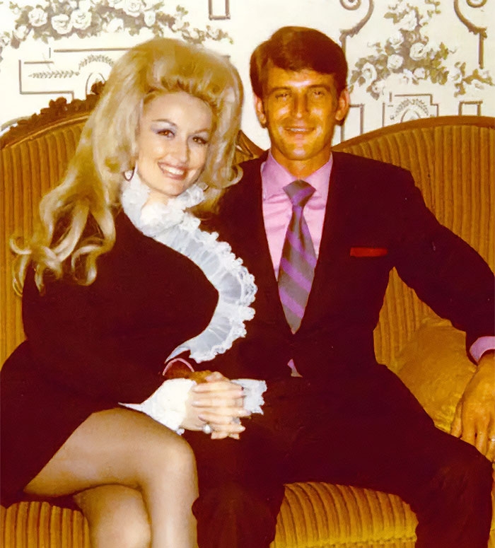 Couple sitting together on a vintage couch, both smiling warmly at the camera.