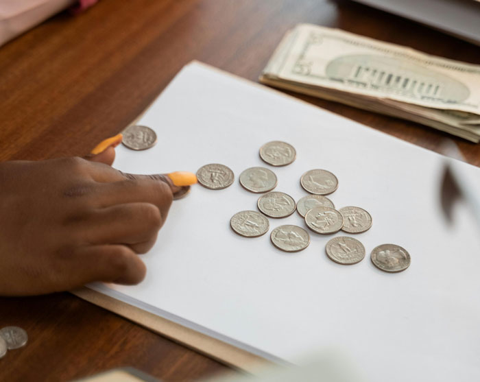 Person counting coins on a table next to money, illustrating a driver&rsquo;s petty revenge over paid tolls.