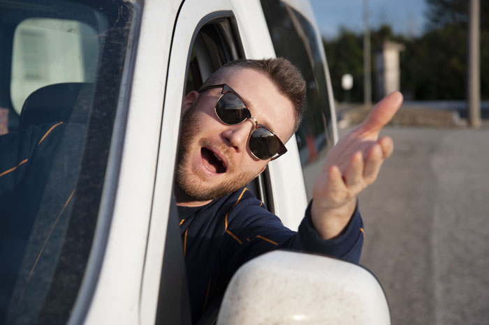 Driver in sunglasses leaning out car window, gestures with a smug expression, illustrating petty revenge.