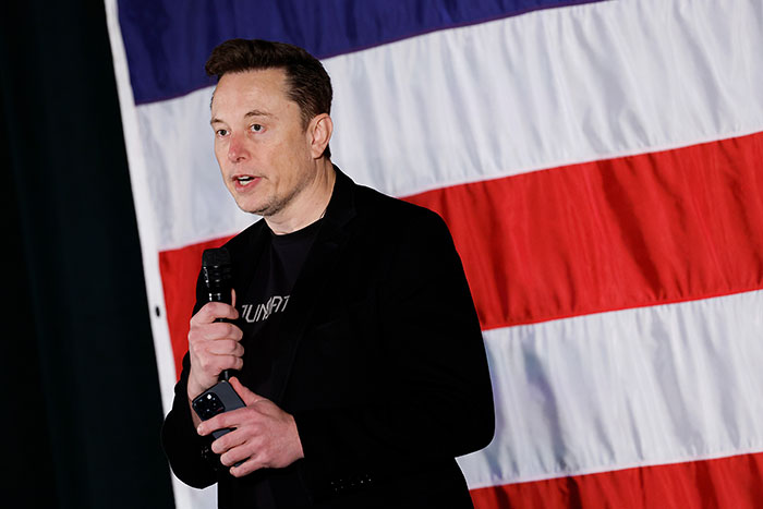 Man speaking with microphone in front of a large American flag, related to SpaceX rescue mission delay.