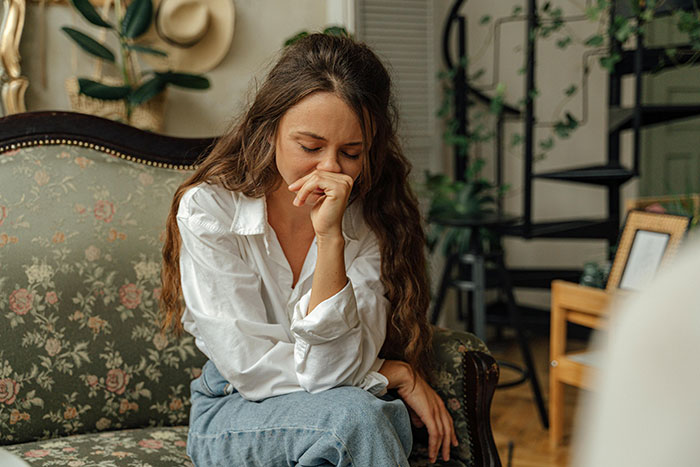 Woman looking worried, sitting on a floral couch, hand to face.