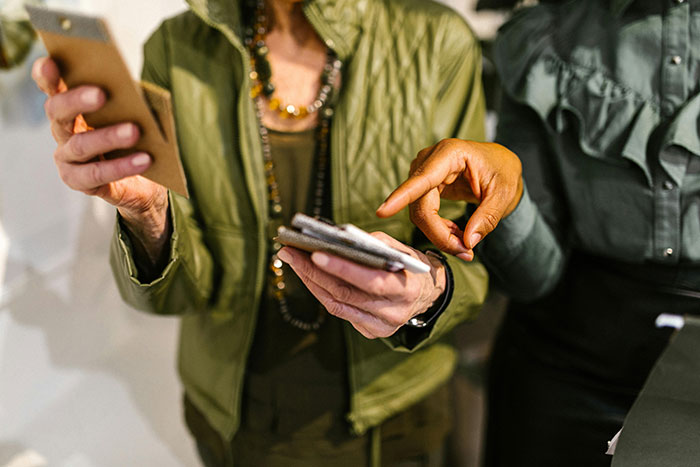 Two women in stylish outfits discussing an influencer trip on their smartphones.