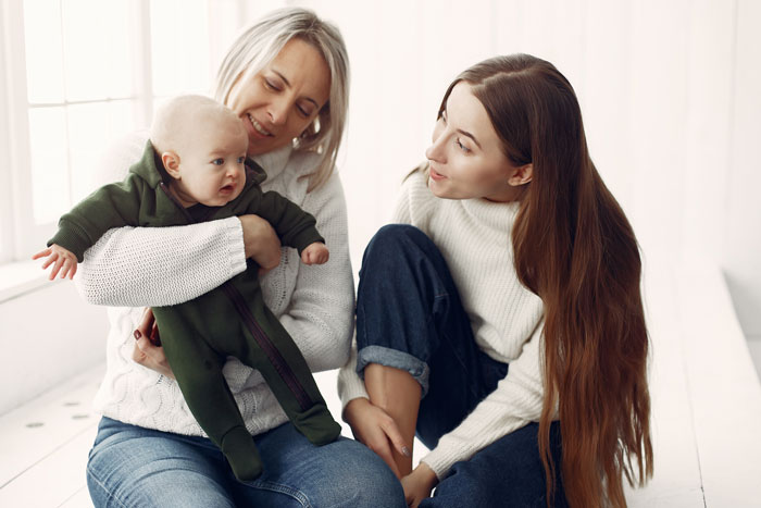 Woman interacting with family, holding a baby, highlighting feelings of exclusion.