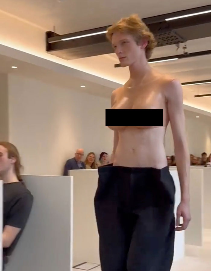 Model in bold outfit at Paris Fashion Week, wearing male top imitating female bare chest.