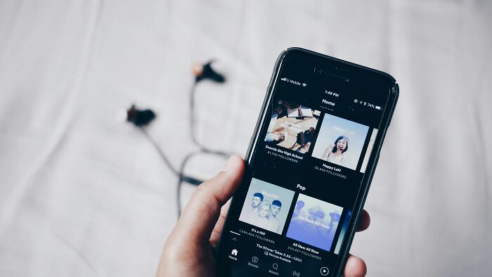 Hand holding a smartphone displaying music streaming app, symbolizing valuable memberships.