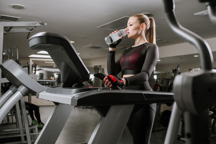 Woman drinking water on a treadmill in a gym, exemplifying valuable fitness memberships.