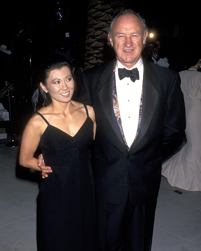 Gene Hackman's daughter, in a black dress, poses with a man in formal attire at an event.