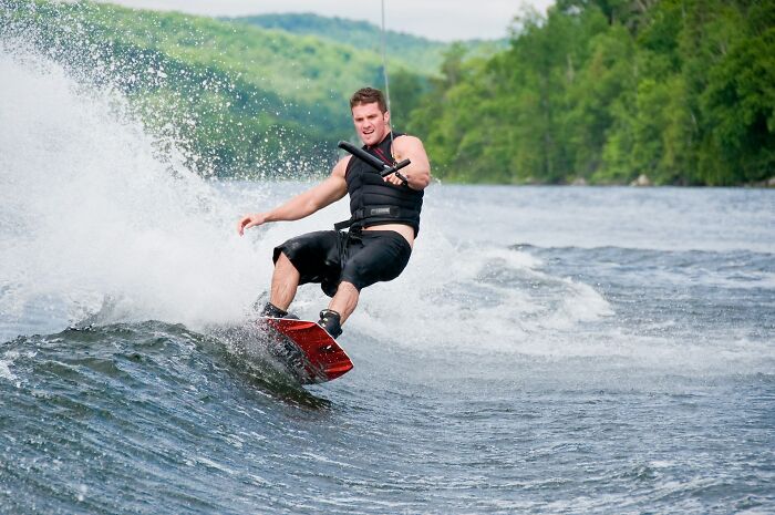 A man wakeboarding on a lake, surrounded by splashing water and greenery.