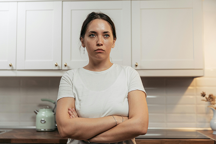 Woman planning a silent exit after uncovering boyfriend’s infidelity, standing with arms crossed in a kitchen.