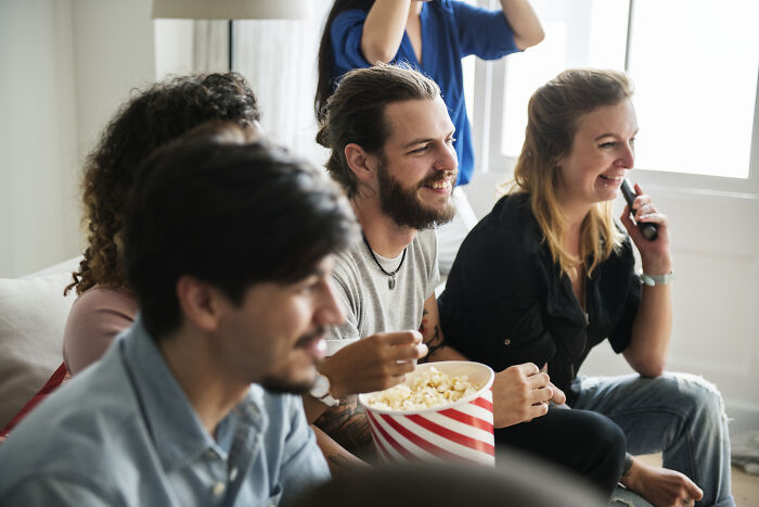 Friends laughing and enjoying popcorn, sitting together on a couch, highlighting the impact of social gatherings.