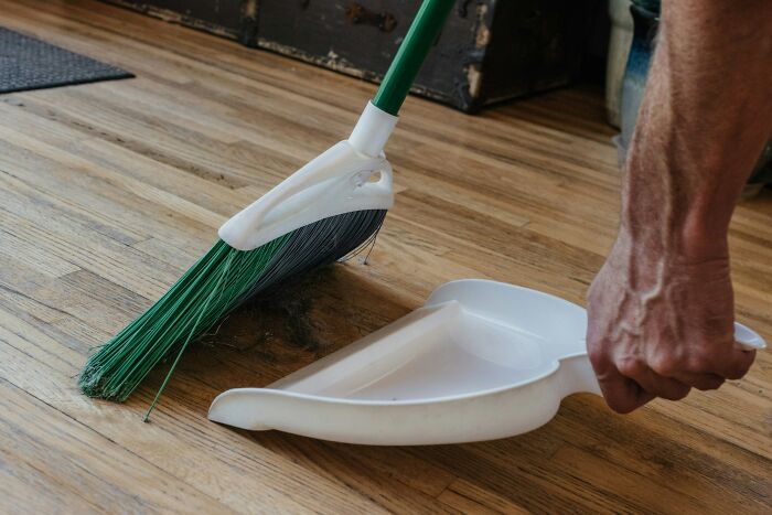 A person using a broom and dustpan to clean a wooden floor, highlighting impactful cleaning hacks.